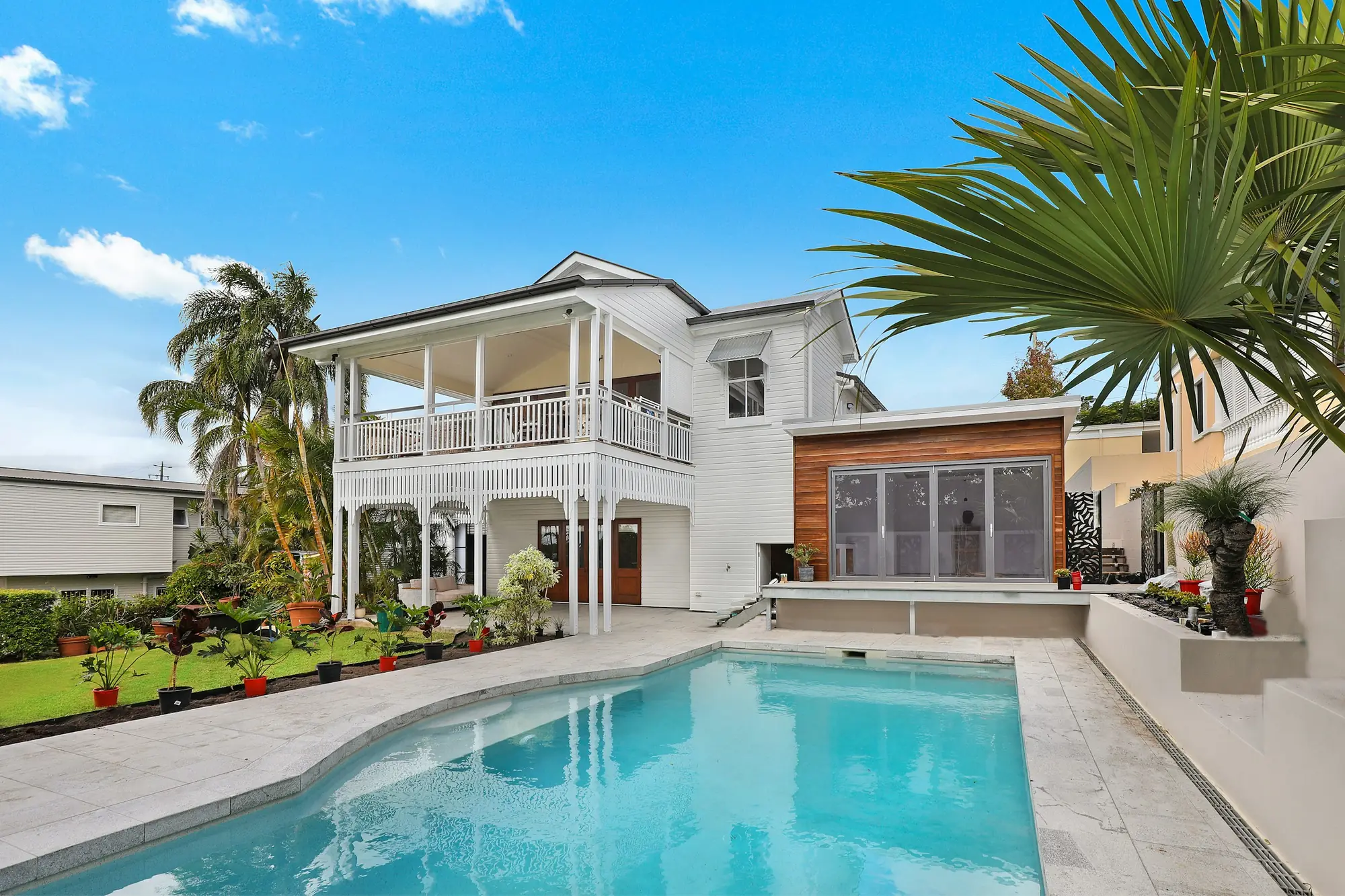 Two story white home with a wraparound balcony, palm trees and a pool